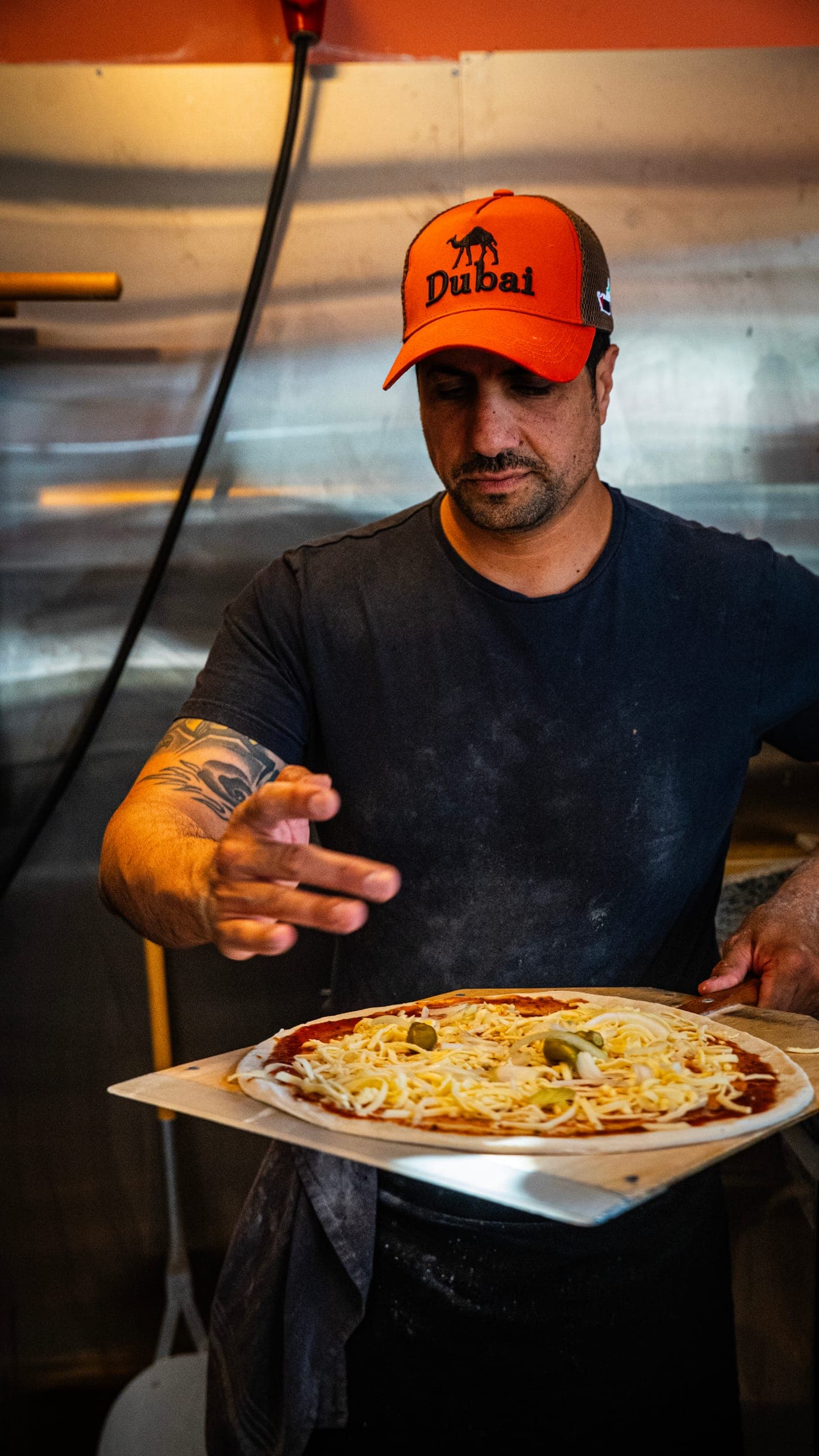 Pizzabagare i orange keps lägger toppning på en pizza i restaurangkök