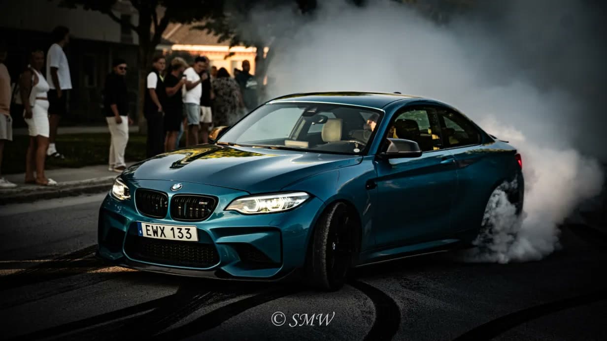 Blågrön BMW gör en burnout omgiven av däckrök framför publik på Slite Expo